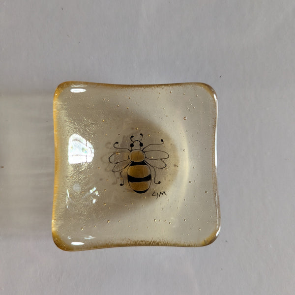 Square glass dish with a bee design on a plain background